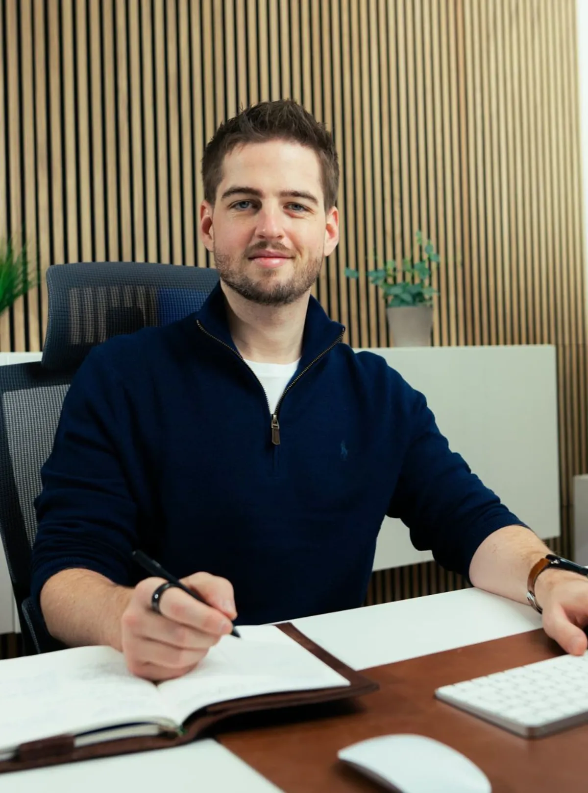 Tim Gelhausen im dunkelblauen Pullover am Schreibtisch, er schreibt in ein Notizbuch
