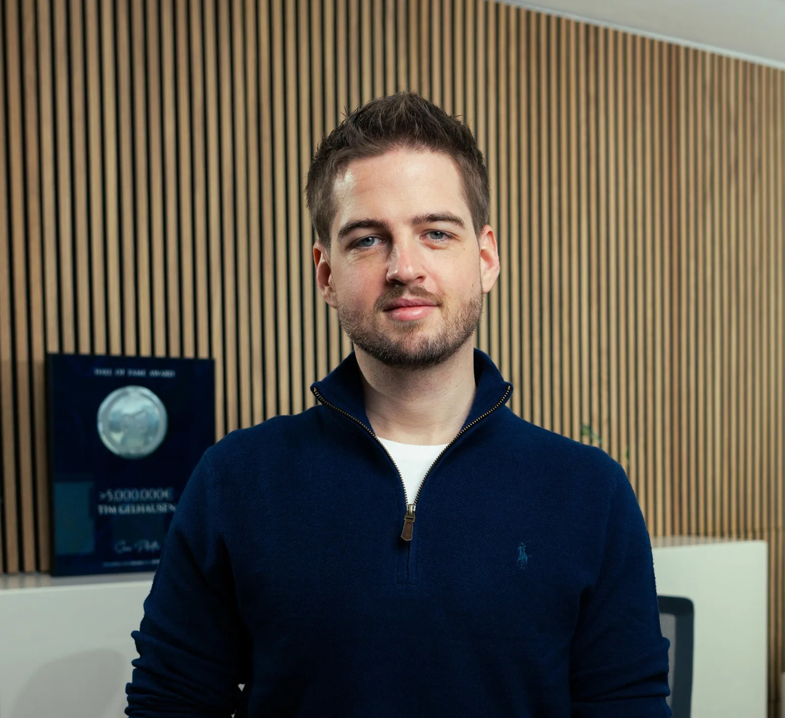 Tim Gelhausen im dunkelblauen Pullover vor einer Holzwand in seinem Büro